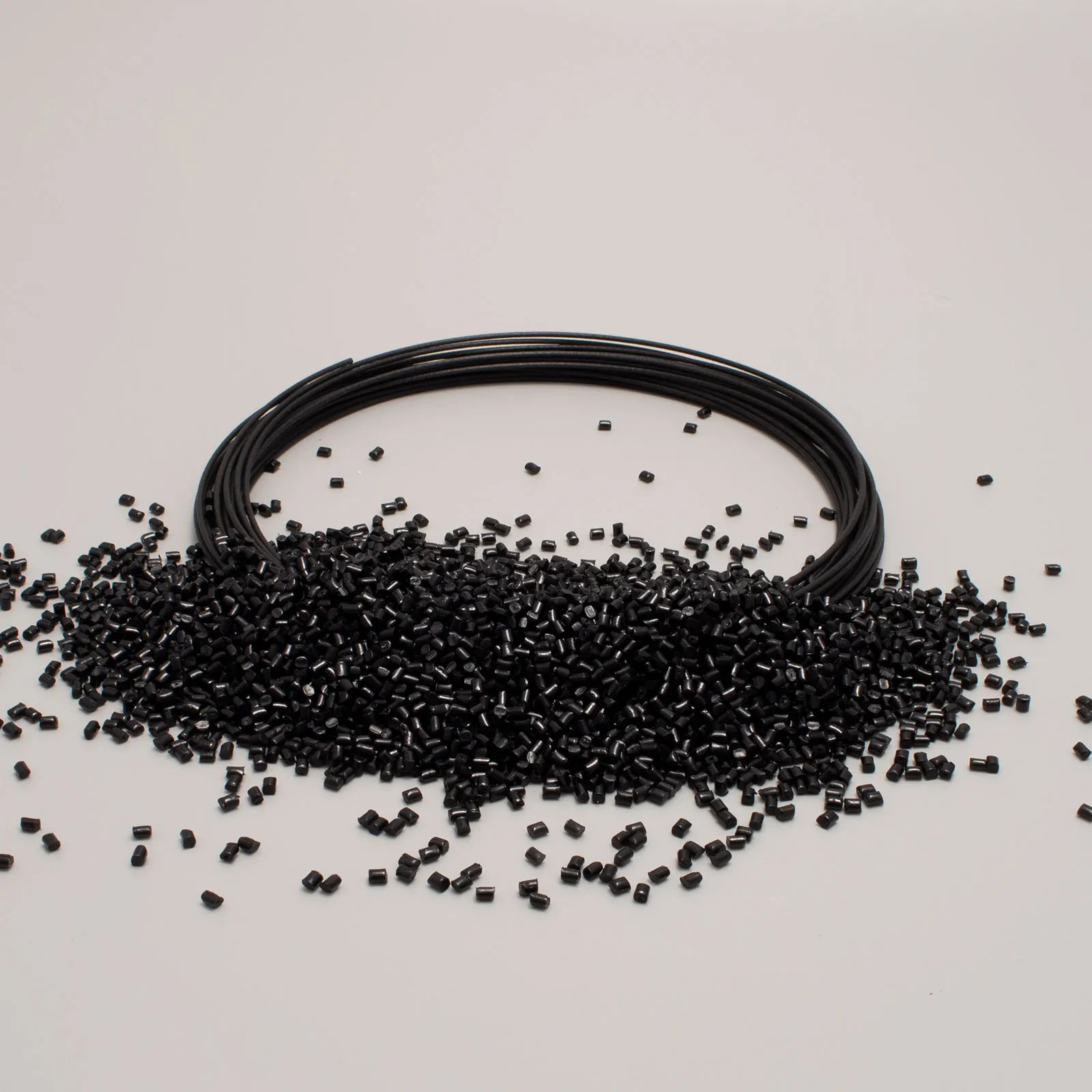 Black plastic wire coil with granules scattered on a white surface, material for 3D printers.
