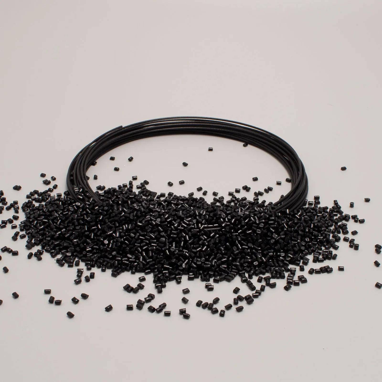 Bobina e granuli di filamento nero per stampa 3D su sfondo bianco.
