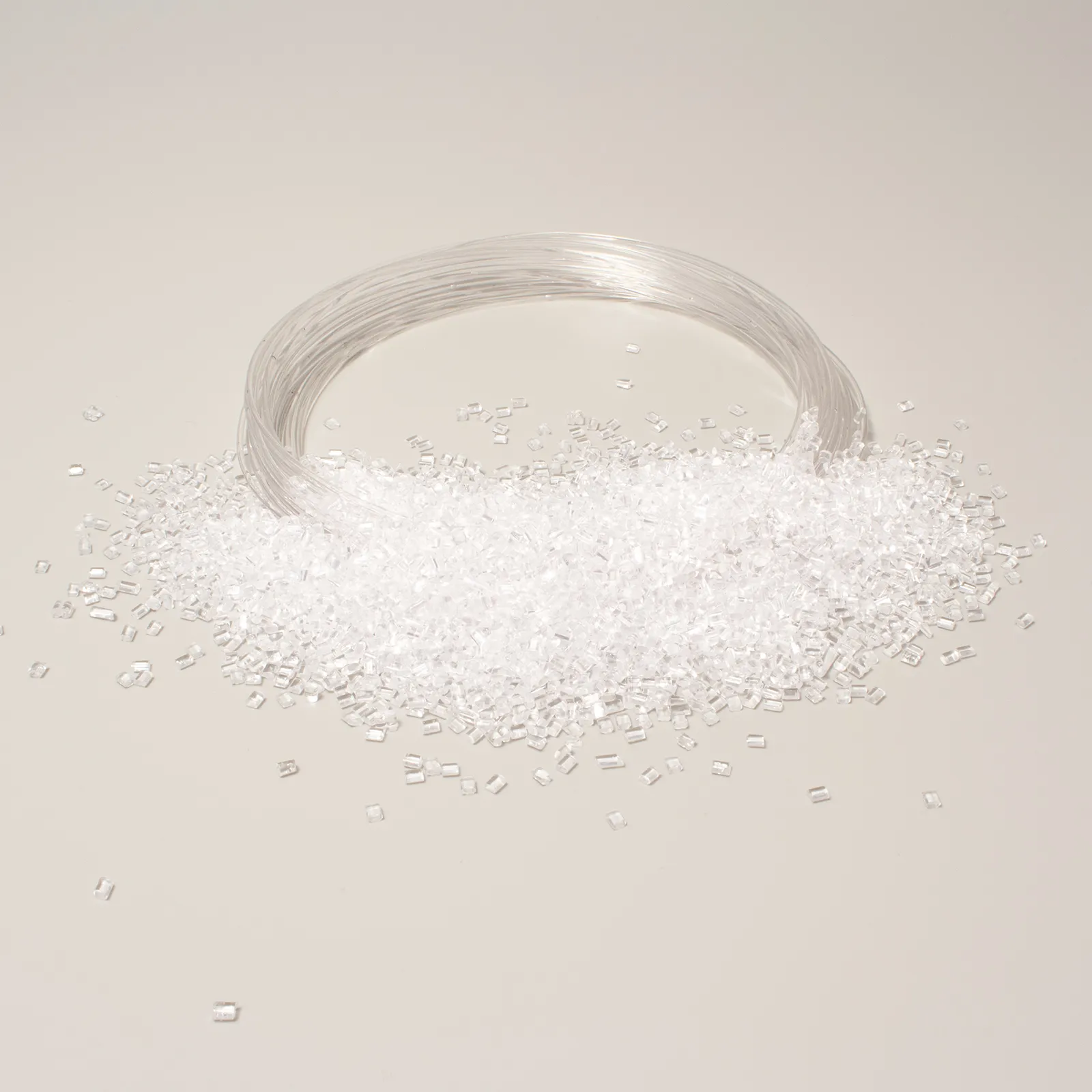 Granuli di plastica traslucida e filo trasparente su fondo neutro per uso industriale o manifatturiero.