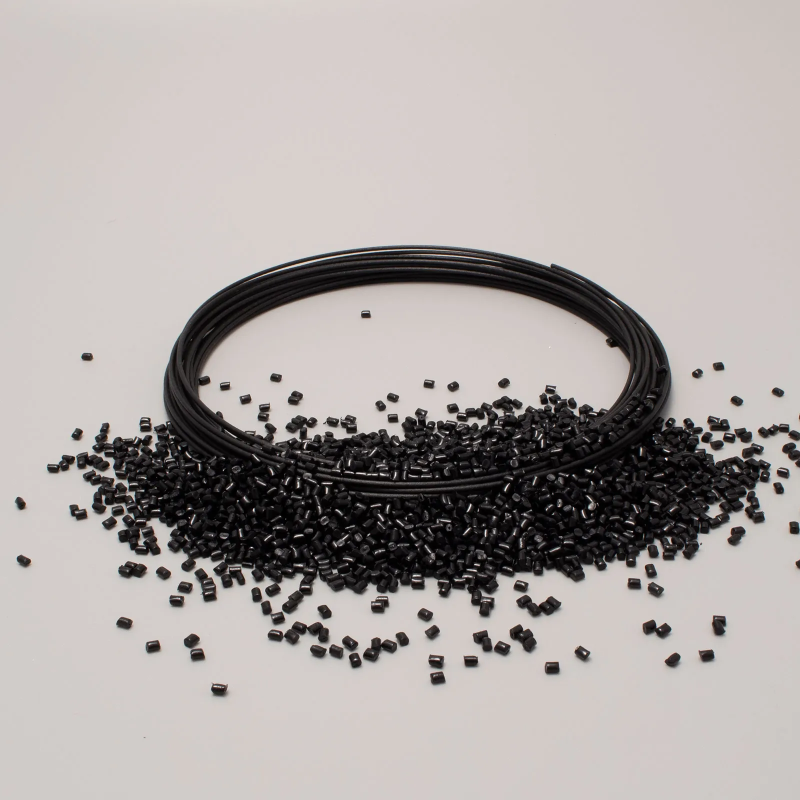 Spool of black filament surrounded by black plastic granules on a white background.