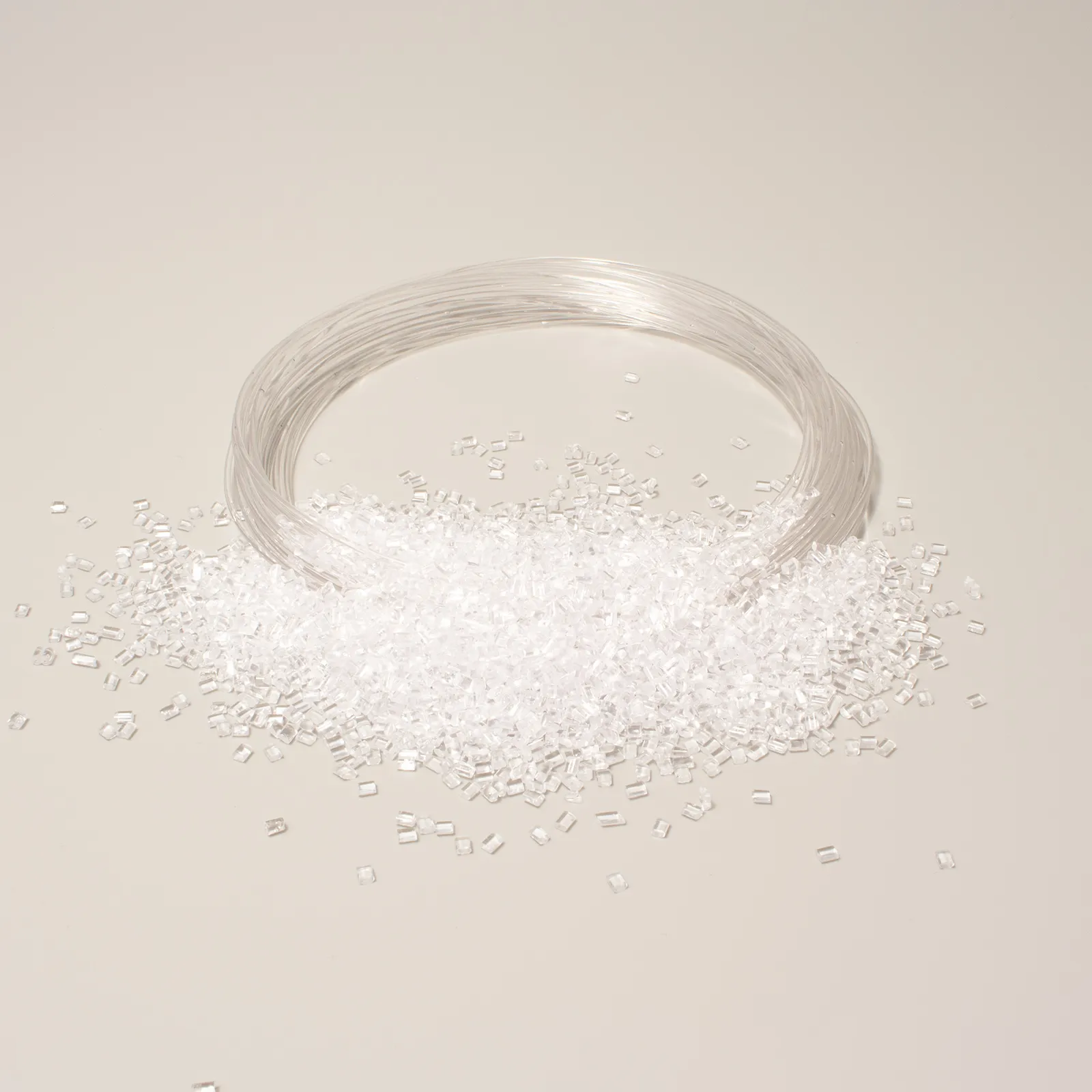 Granuli e filo di polimero trasparente su sfondo chiaro, utilizzati per stampaggio e produzione plastica.