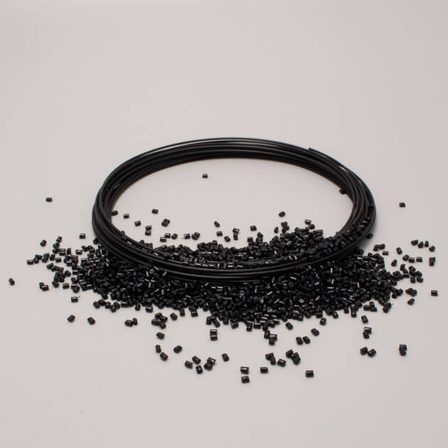Black filament spool for 3D printer with plastic pellets, on a light white background.