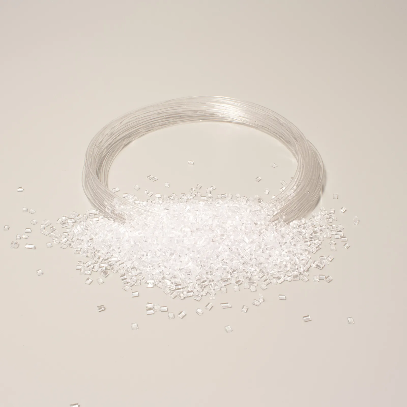 Bobina di filo trasparente circondata da granuli di plastica su sfondo neutro.