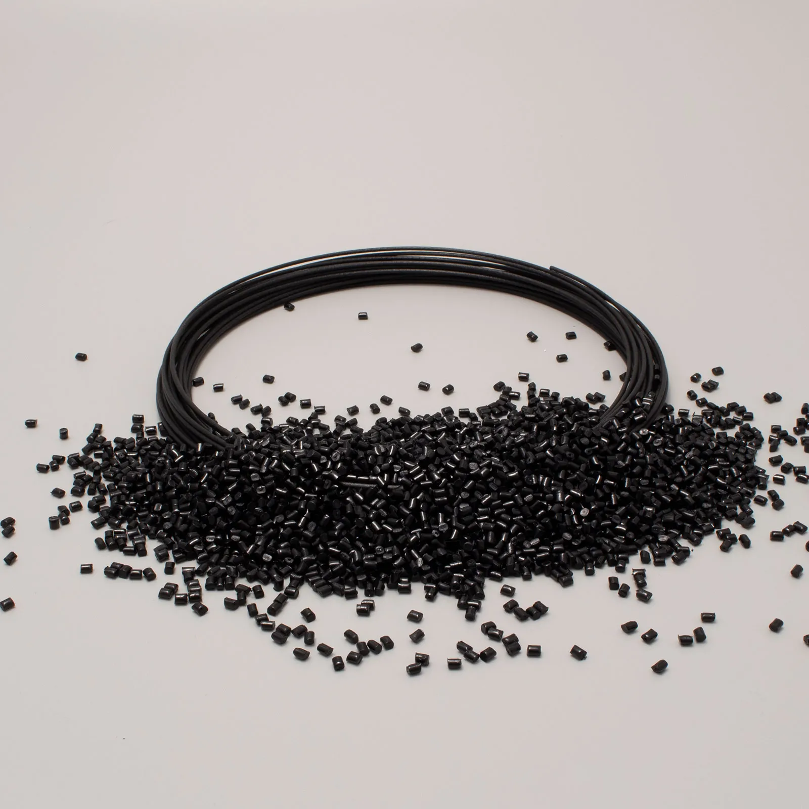 Bobina di filamento nero con granulato su sfondo bianco, utilizzato nella stampa 3D.