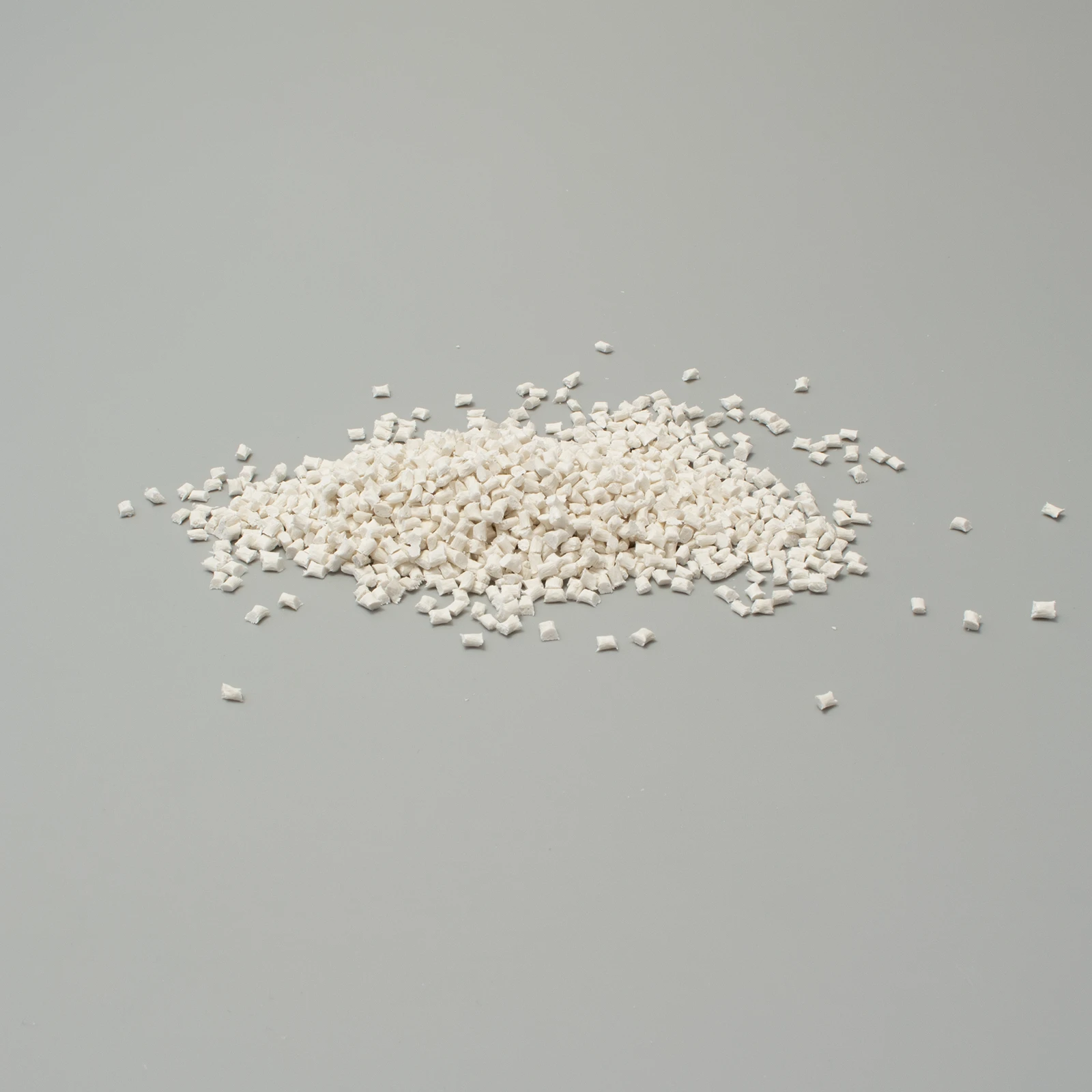 Granuli di plastica bianca su sfondo grigio, utilizzati nella produzione di materiali plastici.