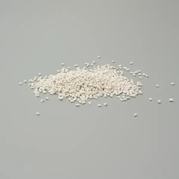 Granuli di plastica bianchi su superfice grigia, usati in produzione industriale e manifatturiera.