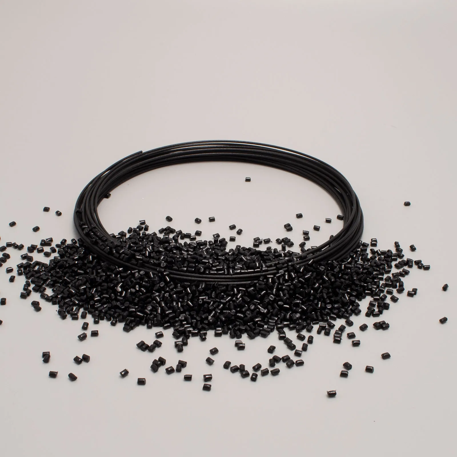 Bobina di filo nero circondata da granuli neri su superficie bianca, ideale per stampa 3D.