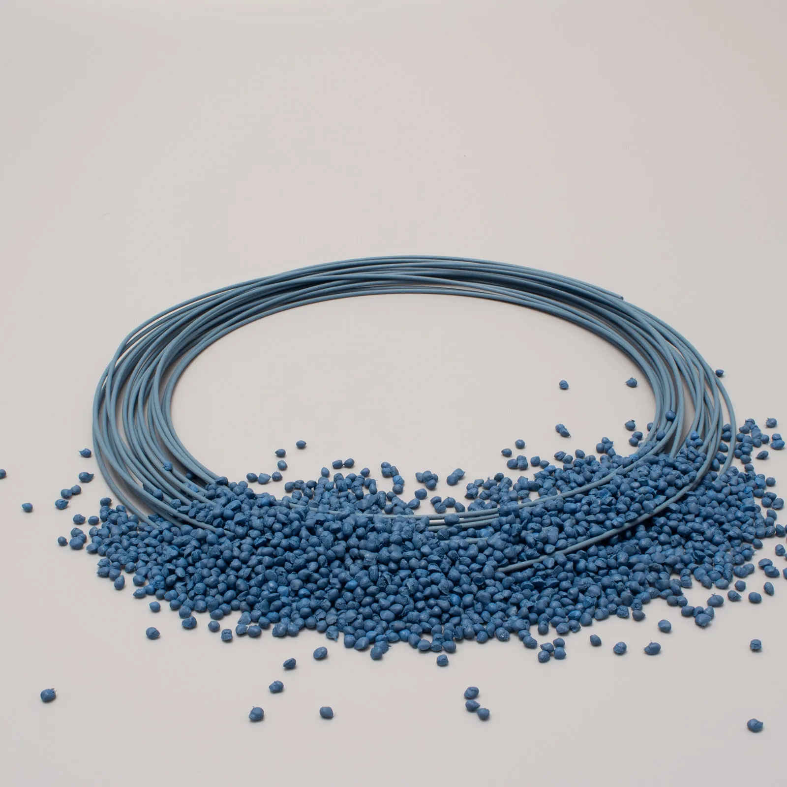 Bobina di filo blu e granuli di plastica blu su sfondo bianco.