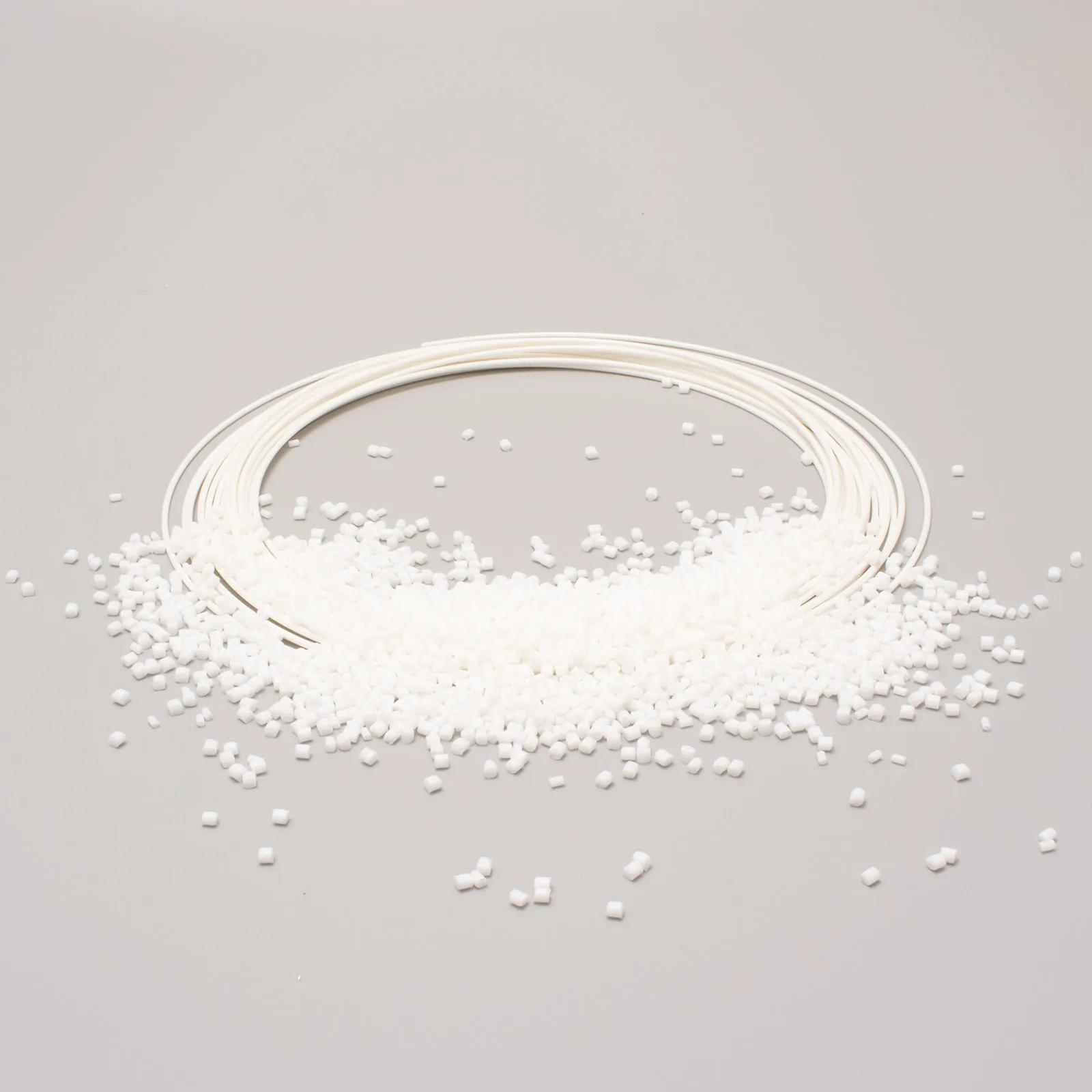 Bobina di filamento bianco circondata da piccoli granuli su sfondo neutro, materiale per stampa 3D.