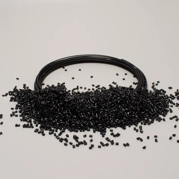 Bobina di filo nero circondata da granuli di plastica nera su sfondo bianco