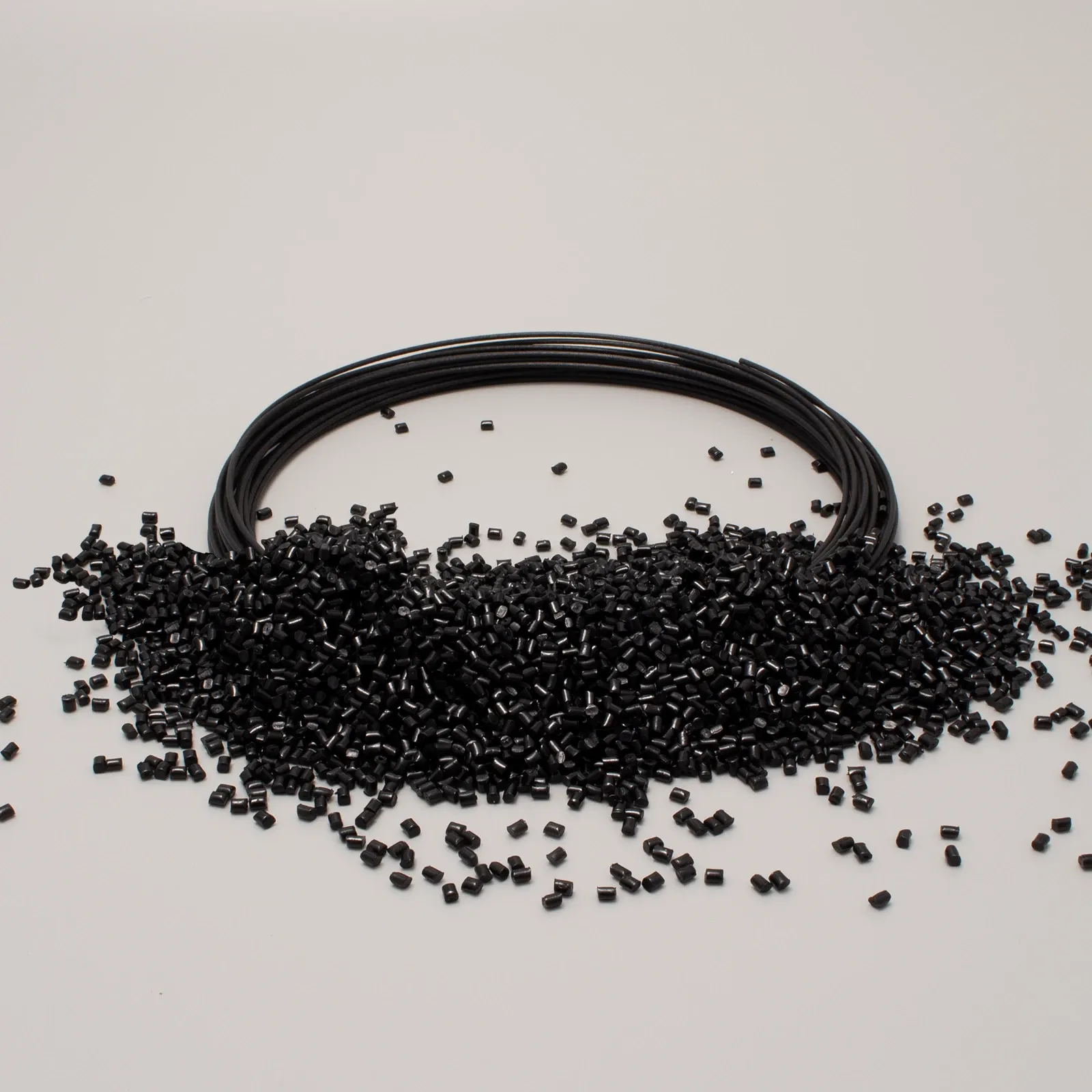 Bobina di filo nero circondata da granuli di plastica nera su sfondo bianco