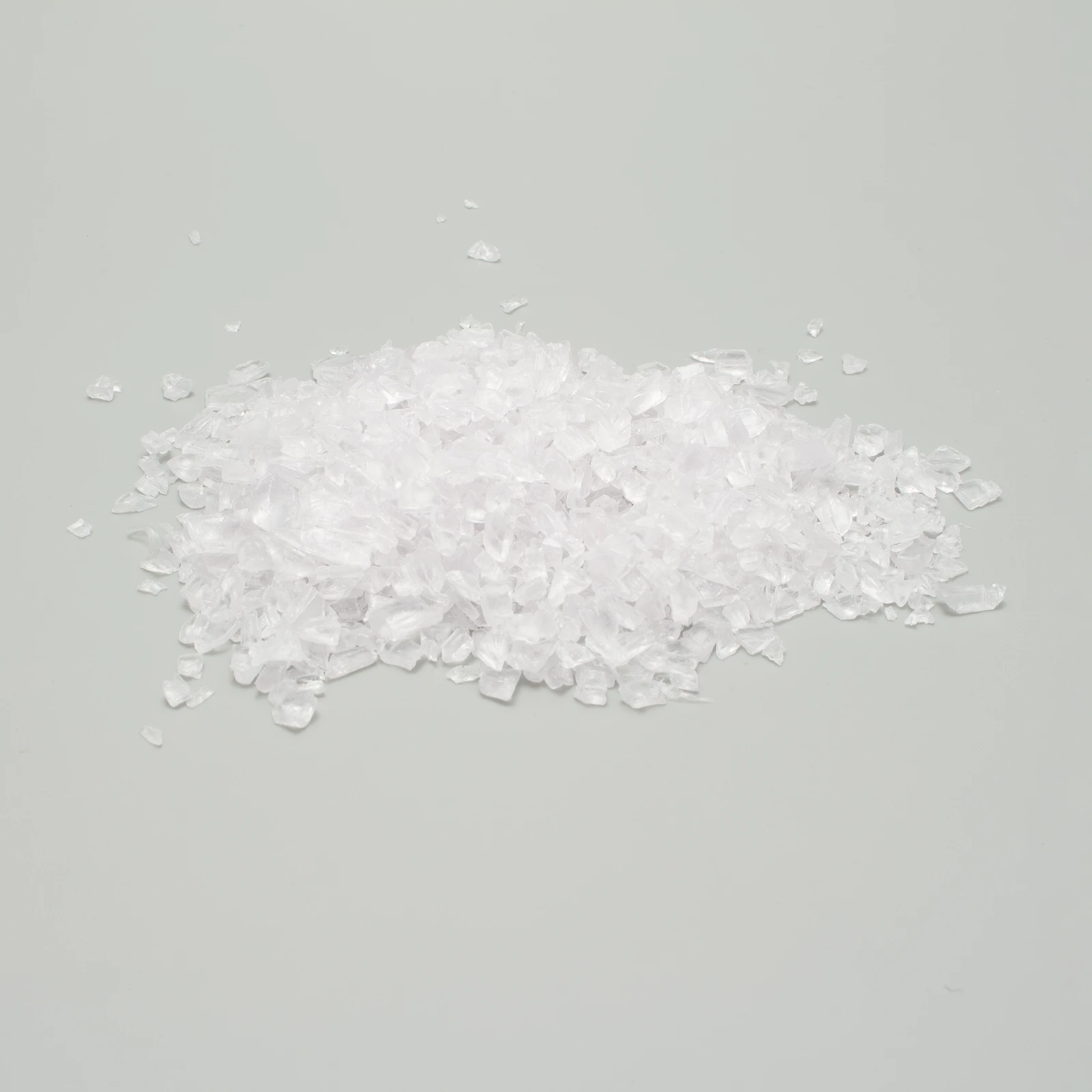 Cristalli di sale grosso bianchi su sfondo grigio chiaro, disposti in un piccolo cumulo centrale.