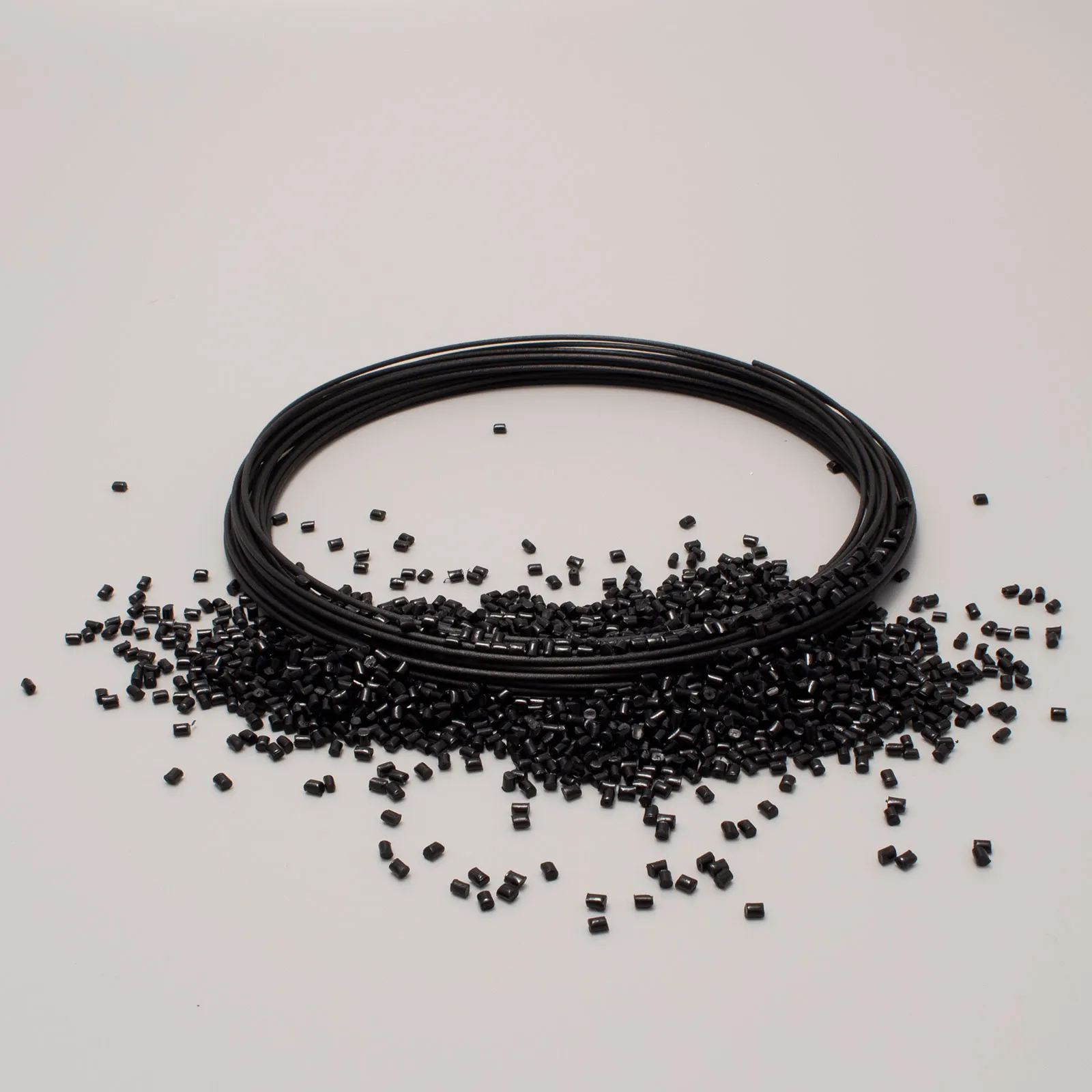 Black filament spool surrounded by small plastic pellets on a light background.
