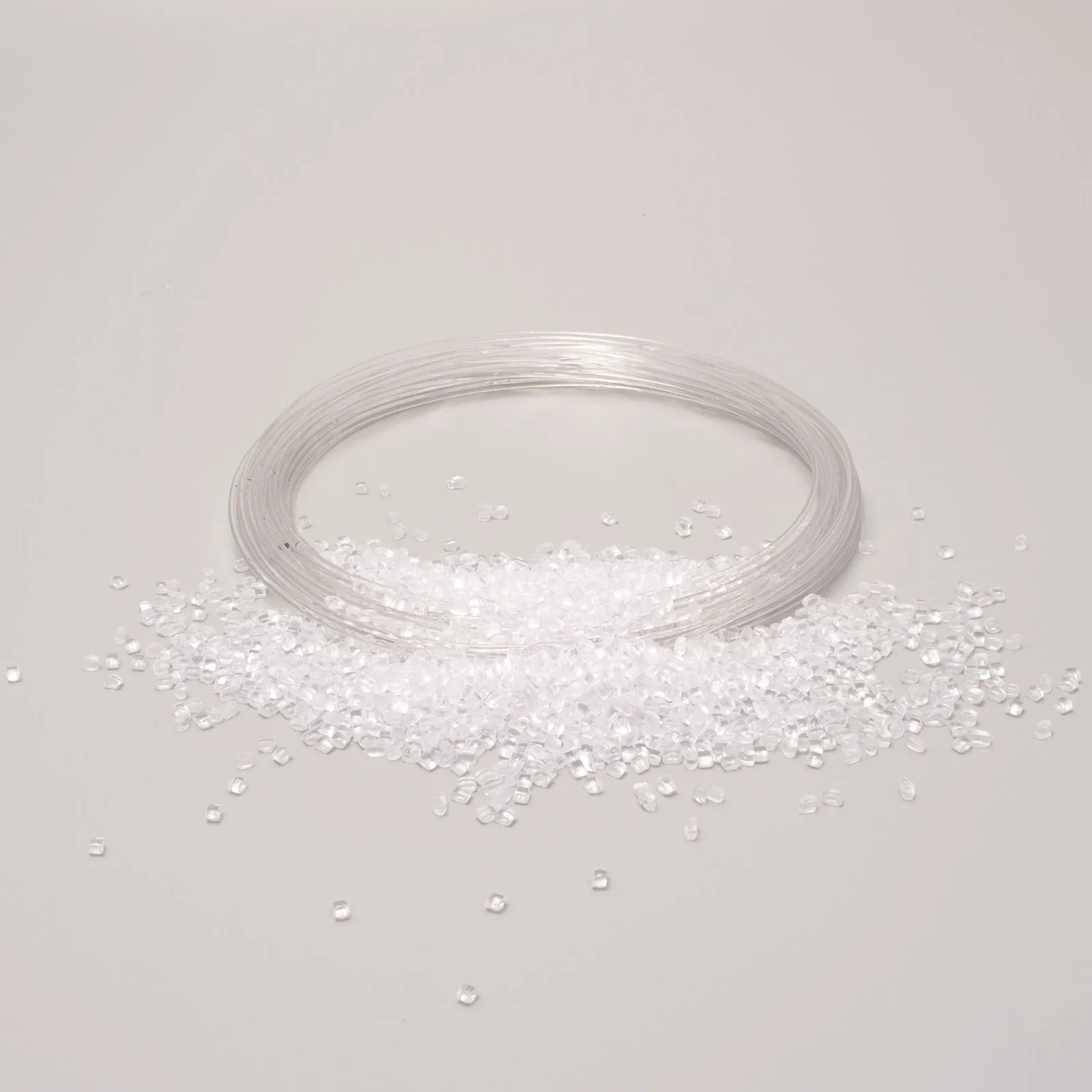 Transparent plastic beads with a loop of plastic filament on a light background, raw material for industrial production.