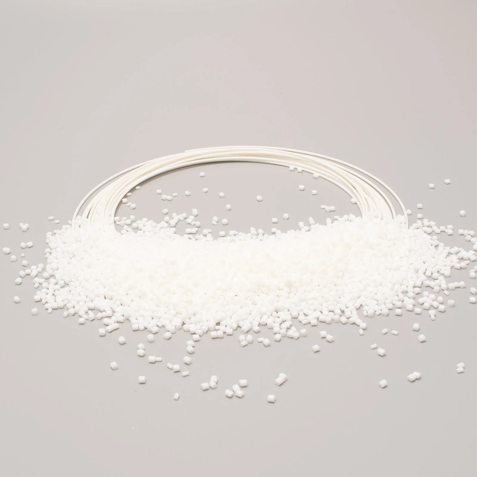 Granuli bianchi di materiale plastico con rotolo di filo bianco su sfondo grigio.