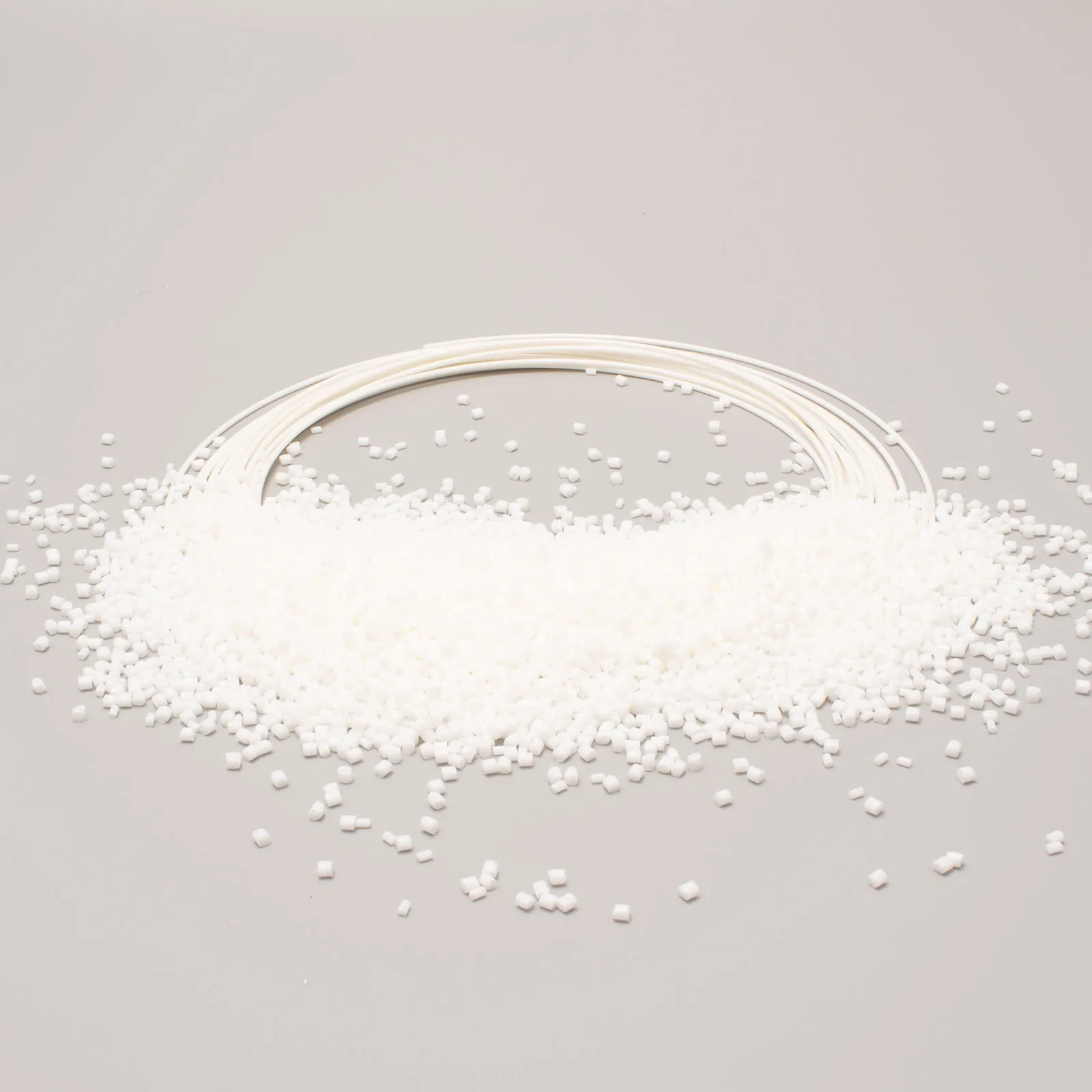 Granuli di plastica bianca sparsi su una superficie, accanto a tubi flessibili bianchi.