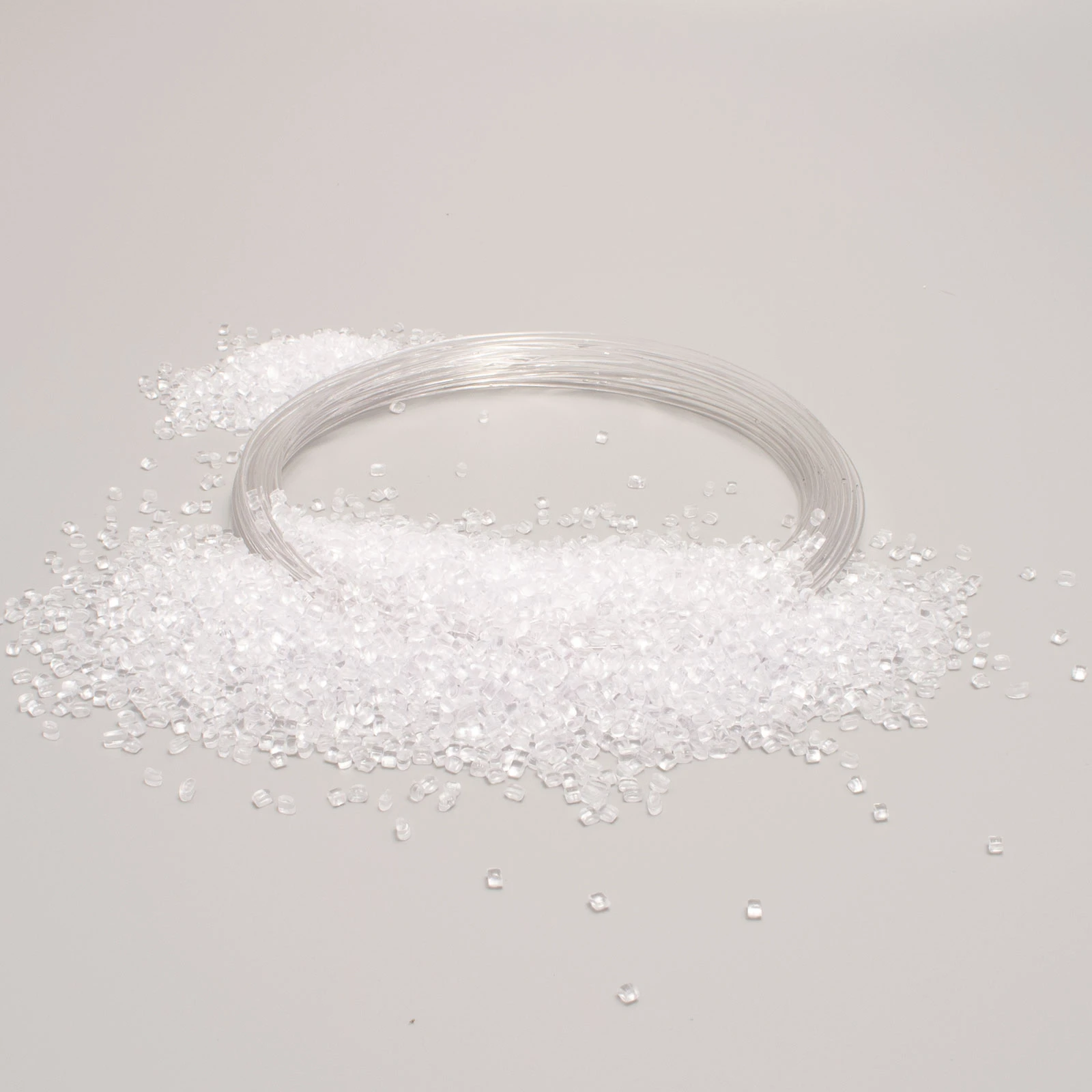 Granuli di plastica trasparente sparsi su un tavolo grigio con un tubo flessibile arrotolato accanto.