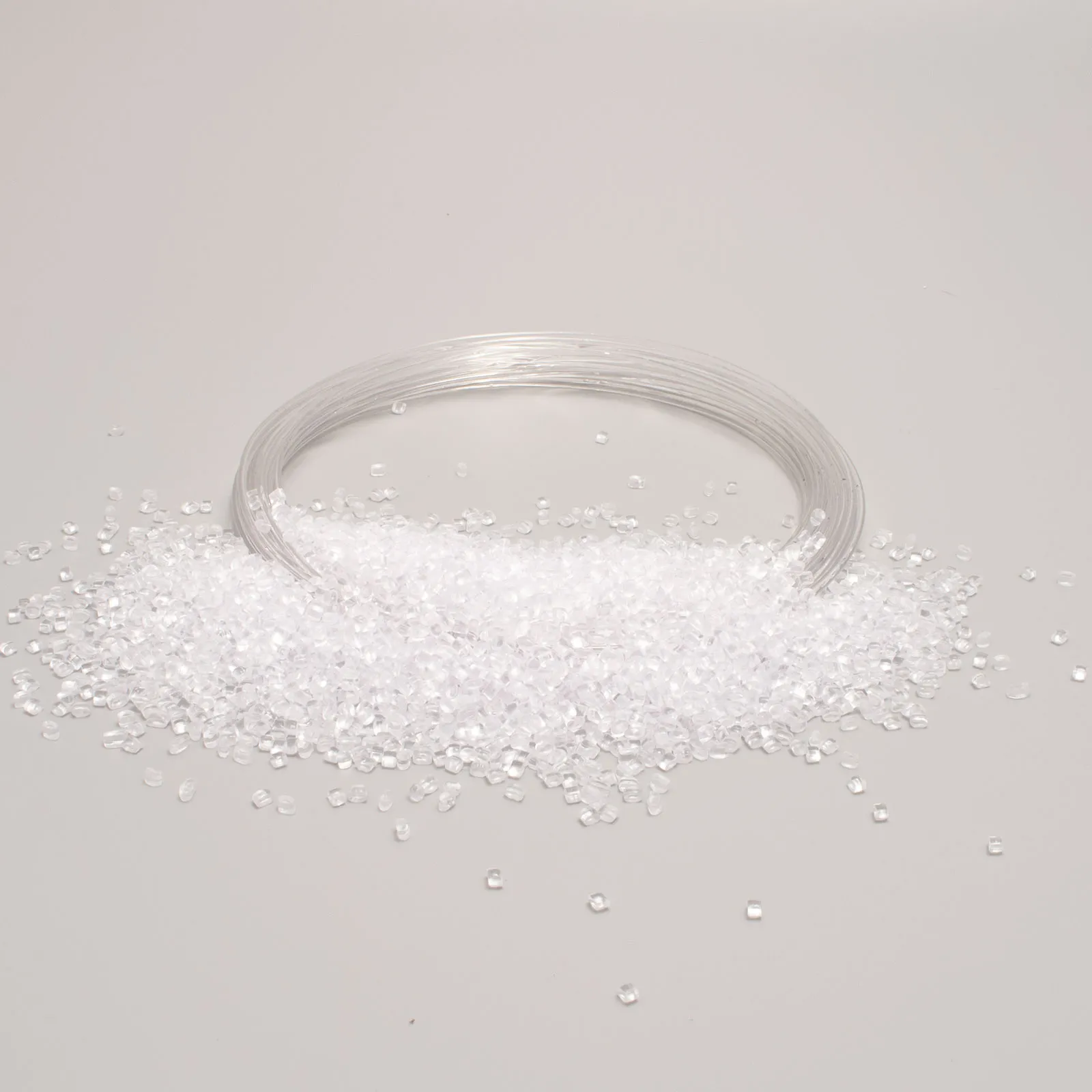 Transparent plastic granules and coiled filament on a white background for industrial and manufacturing use.