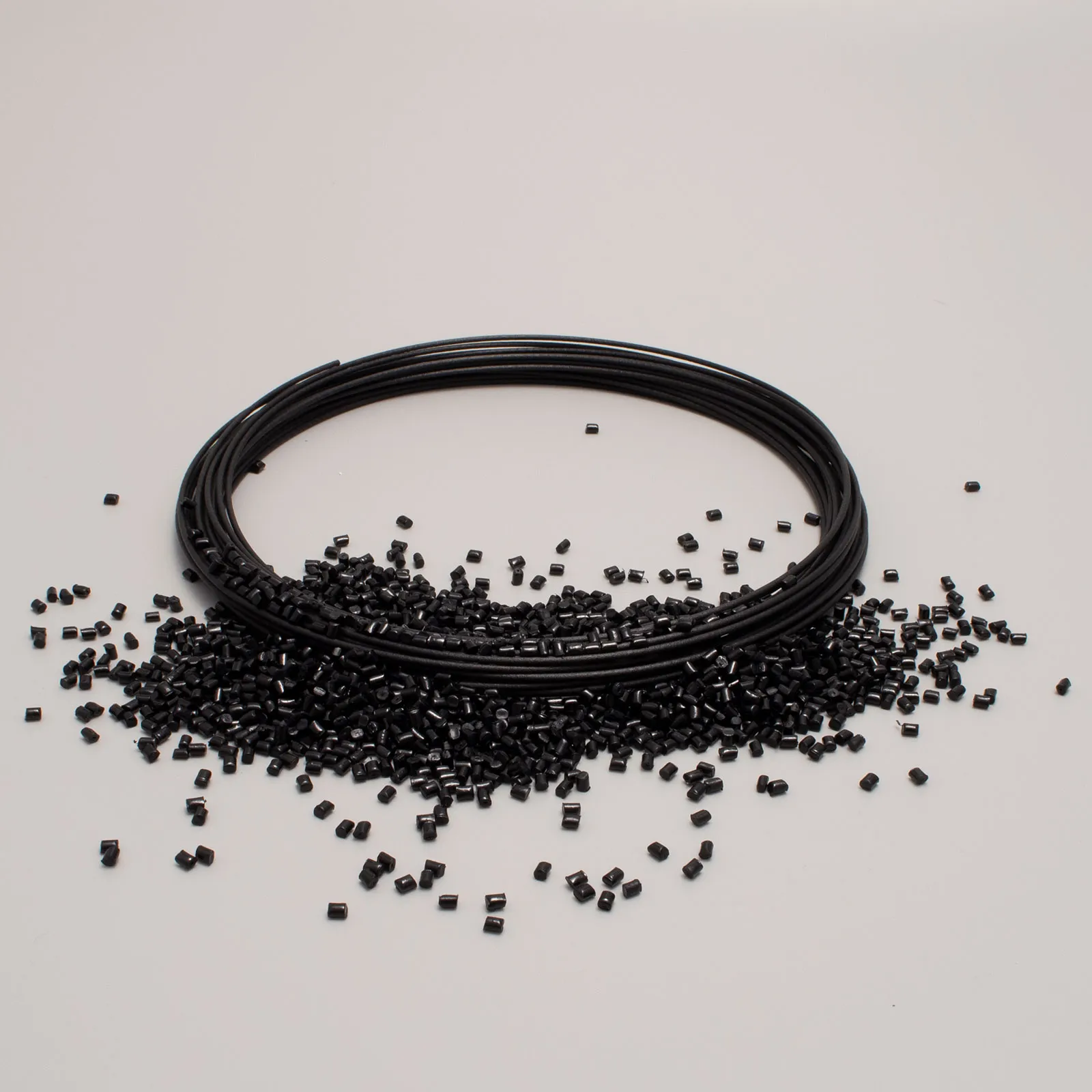 Black 3D printing filament spool with scattered pellets on a light background, representing technical polymers.