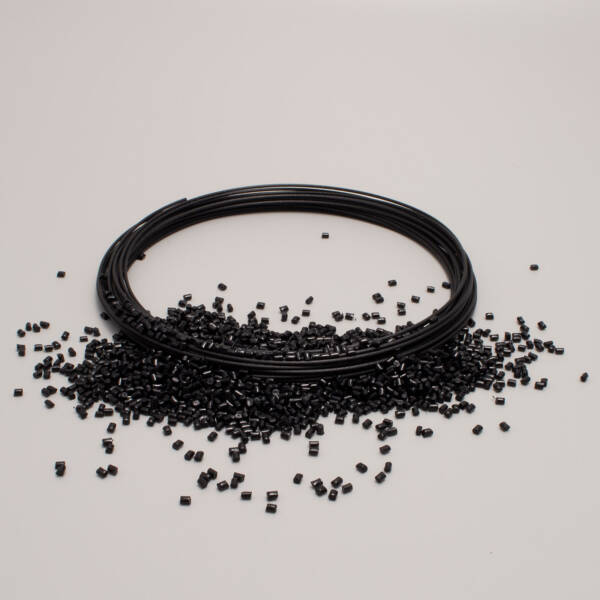Bobina di filo per stampa 3D con pellet di plastica neri sparsi sul pavimento bianco.