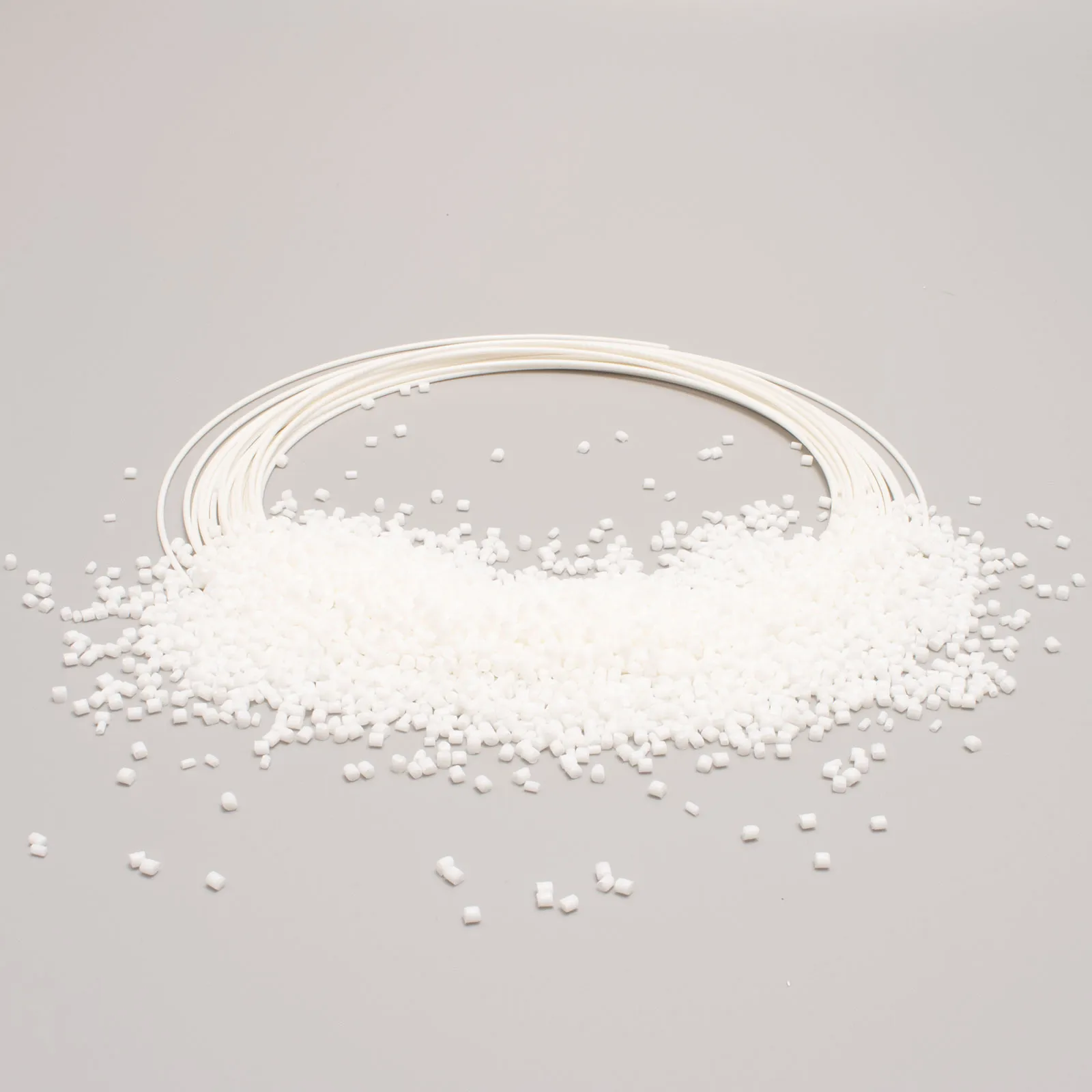 Granuli bianchi di plastica PET e filo in bobina su sfondo neutro, materiale per stampa 3D e produzione.