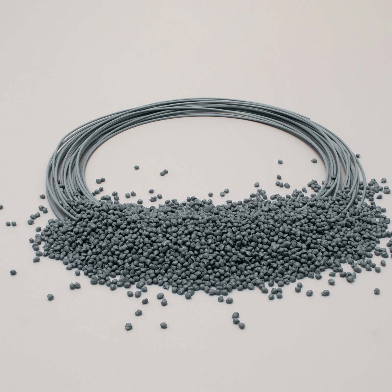 Gray filament spool with piles of small pellets, placed on a light surface.