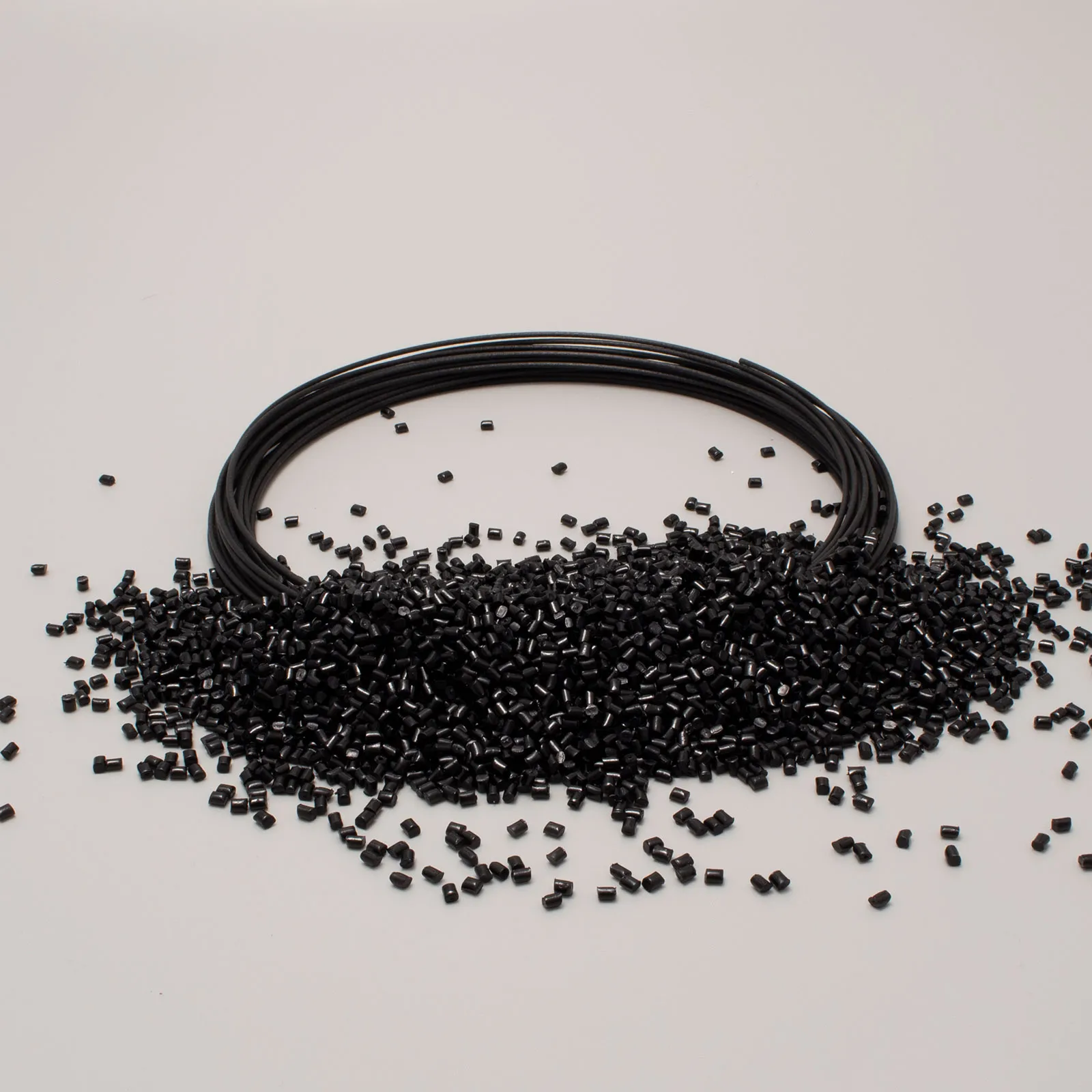 Bobina di filamento nero per stampante 3D con granuli di plastica neri sparsi su fondo chiaro.